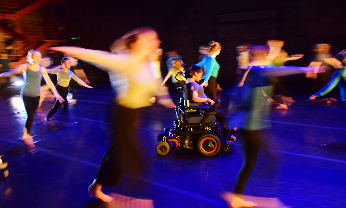 Blurry dancers around a dancer in a wheechair.