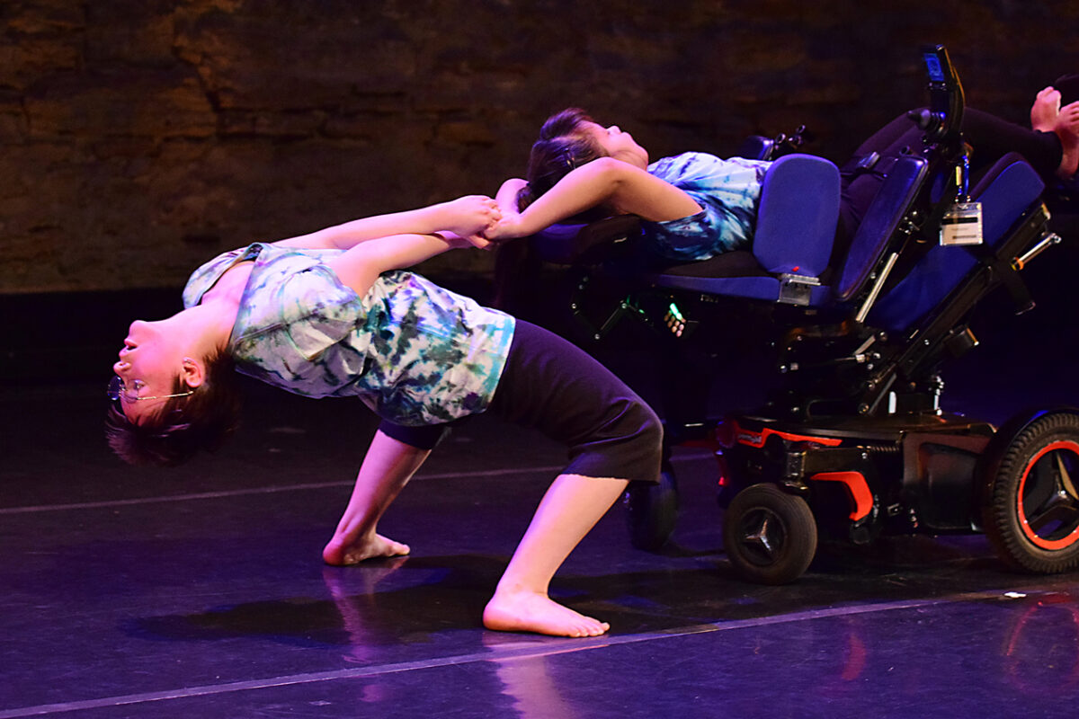 Dancer in extreme dance move with a dancer in a wheelchair.