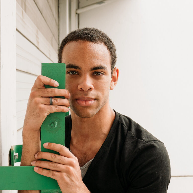 Photo of black man, Javan, holding a green pole and smiling at the camera.