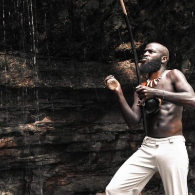 Black man Guerreiro in front of a waterfall while dancing.
