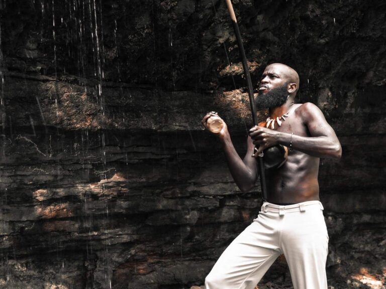 Black man Guerreiro in front of a waterfall while dancing.