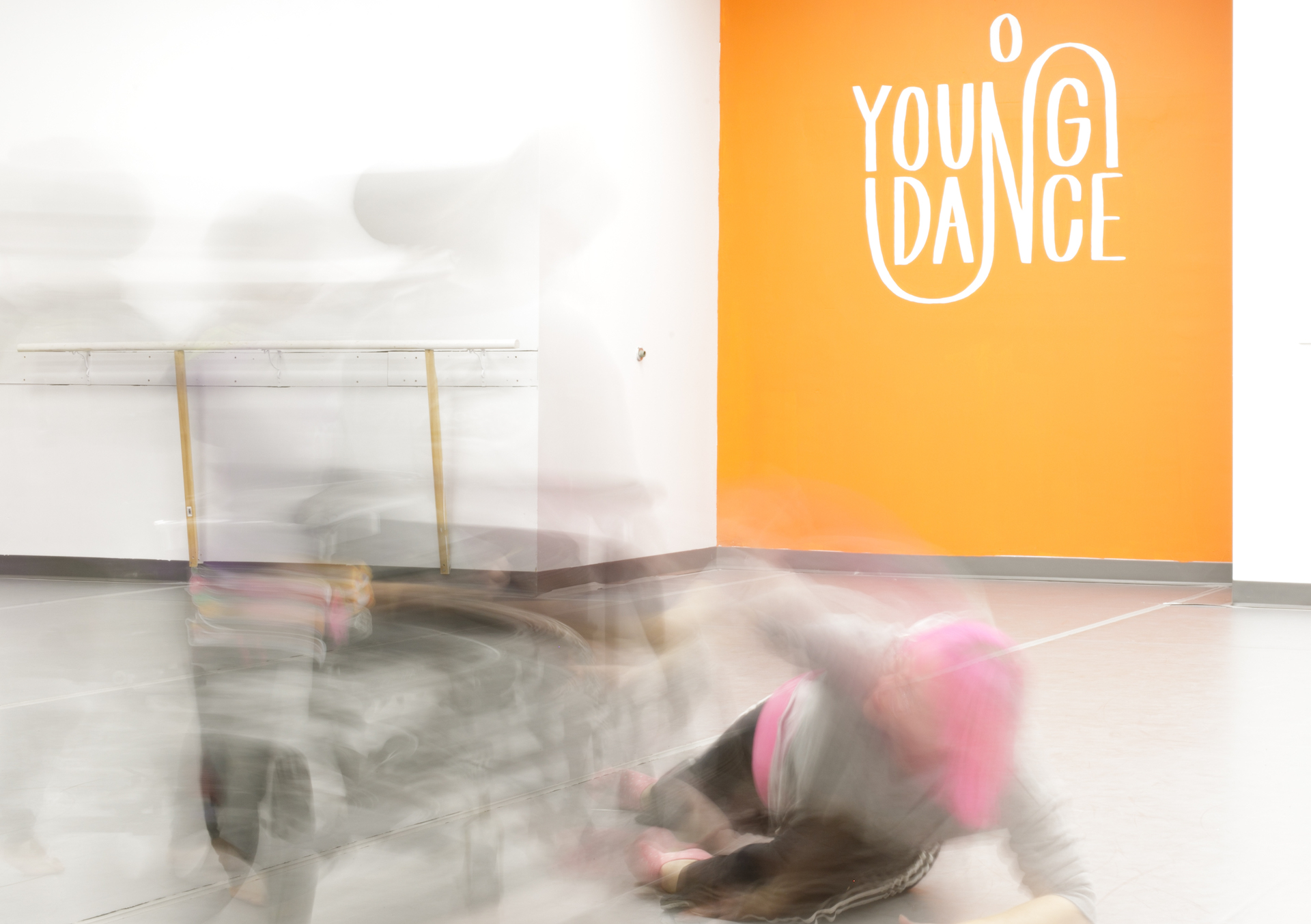 Image of orange studio with blurry dancers. One dancer is in a wheelchair. 