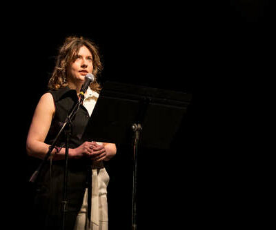 White woman, Emily Gastineau, speaking at a microphone.