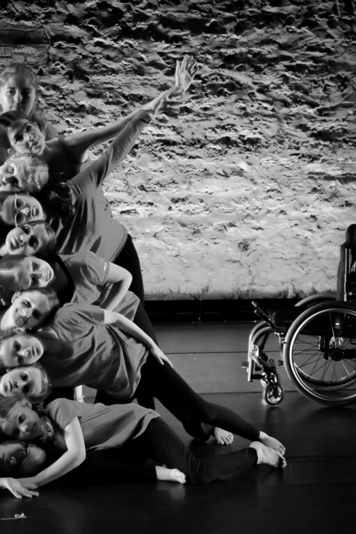 Image of dancers' heads stacked vertically with a wheelchair on the side. 