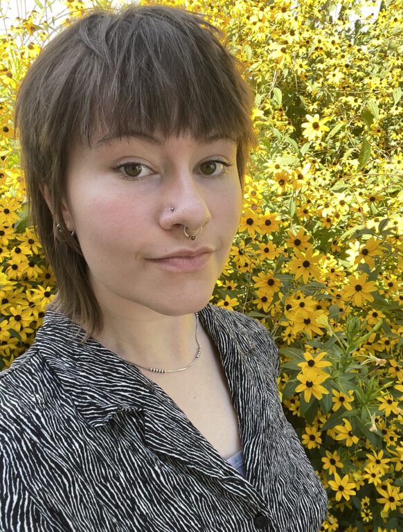 A white woman, Piper Rolfes, posing in front of flowers.