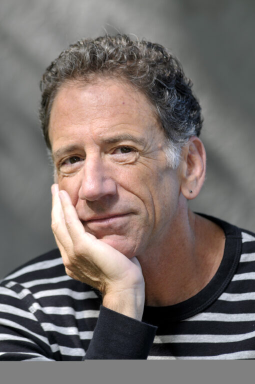 Curly haired white man, Stuart Pimsler, softly smiling with his hand under his chin.