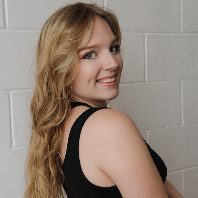 Woman, Mayhugh, with long blond hair smiling over her shoulder.