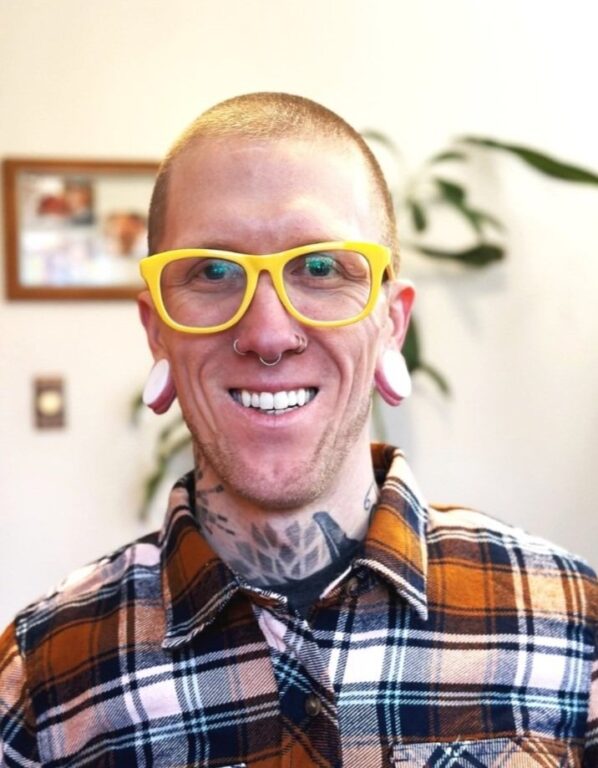 White man in yellow glasses and a plaid shirt, Ryan McLaughlin, smiling.